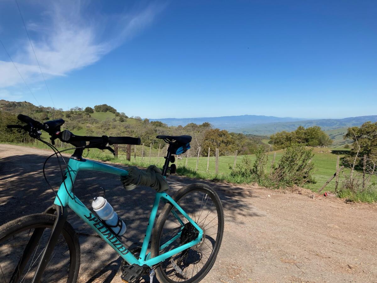 a blue Specialized hybrid bike parked on a hill overlooking green pastures and countryside