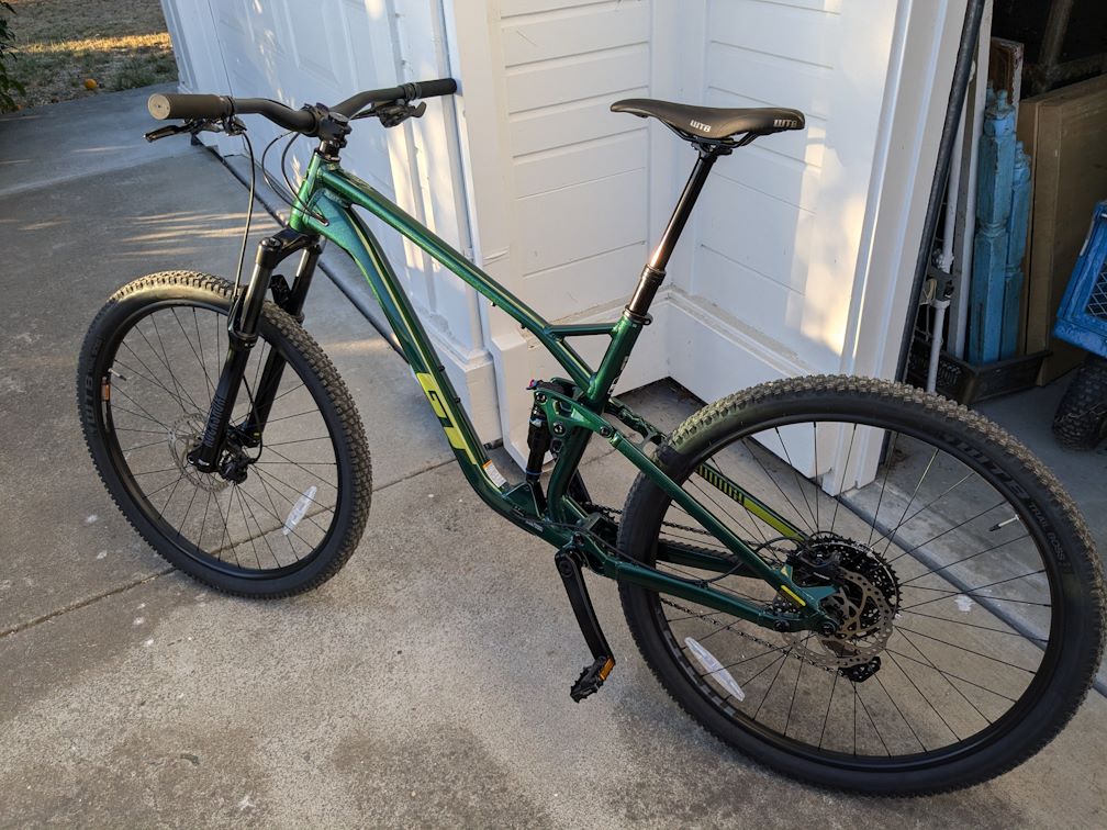 a forest green full suspension GT mountain bike leans against a garage