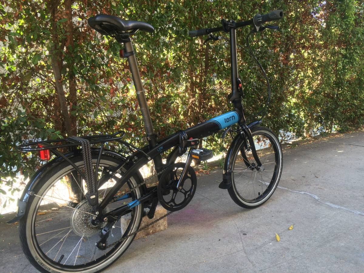 A tern link d8 folding bike in black with blue accents, propped near a fence