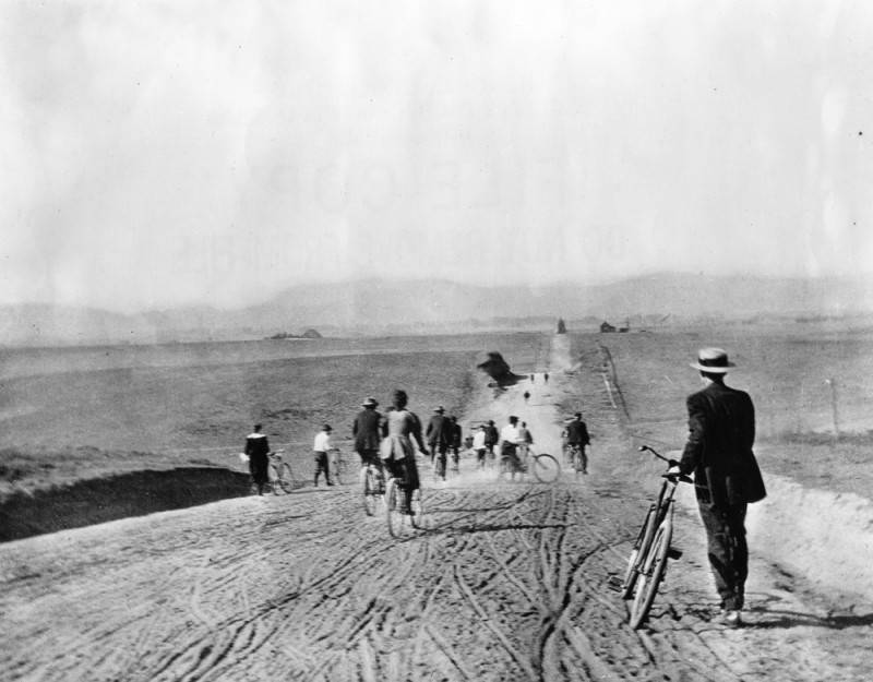 an old photo from the 1900s of people on bikes on rolling hills with dirt roads and scattered farmhouses, in modern day Koreatown, Los Angeles