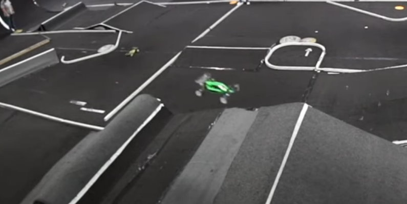 a green and black RC10B4.1 rc buggy is midair on a carpet track