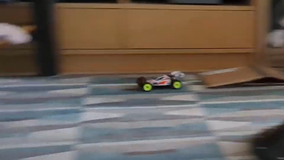 a blurry photo of a kyosho mini-z buggy with optima mid white and orange coloring, driving on a rug