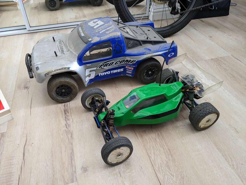 a blue and silver Team Associated SC10 rc short course truck next to a green and black B4.1 buggy on a laminate brown floor