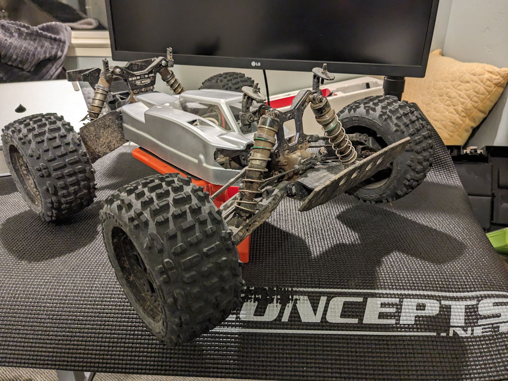 an MT410 rc car is on a car stand on a desk with a 1:8 buggy body on it. It's dirty