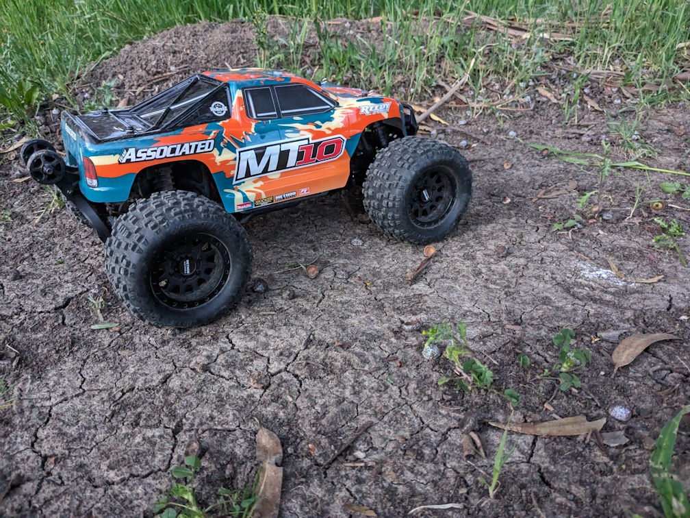 a rival mt10 monster truck from the side on a grassy dirt rc track