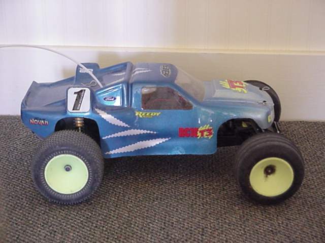 a Team associated RC10T3 rc Stadium Truck with a blue and silver body and yellow wheels on a green carpet floor