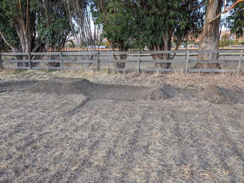 a dry field with brown mowed grass has a tabletop jump and double built in it