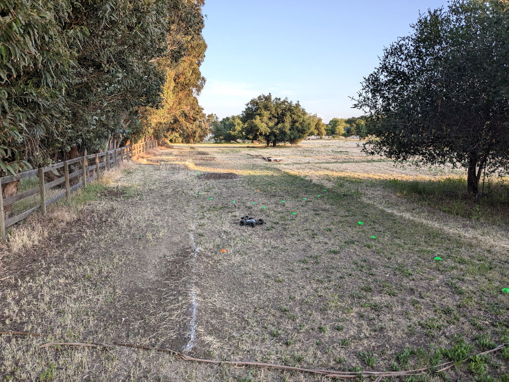 a look from one end down a long dirt rc track, a car is in the foreground near a turn rough motocross style course